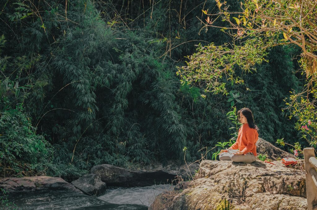Asian woman in orange meditating by a stream in an Asian forest