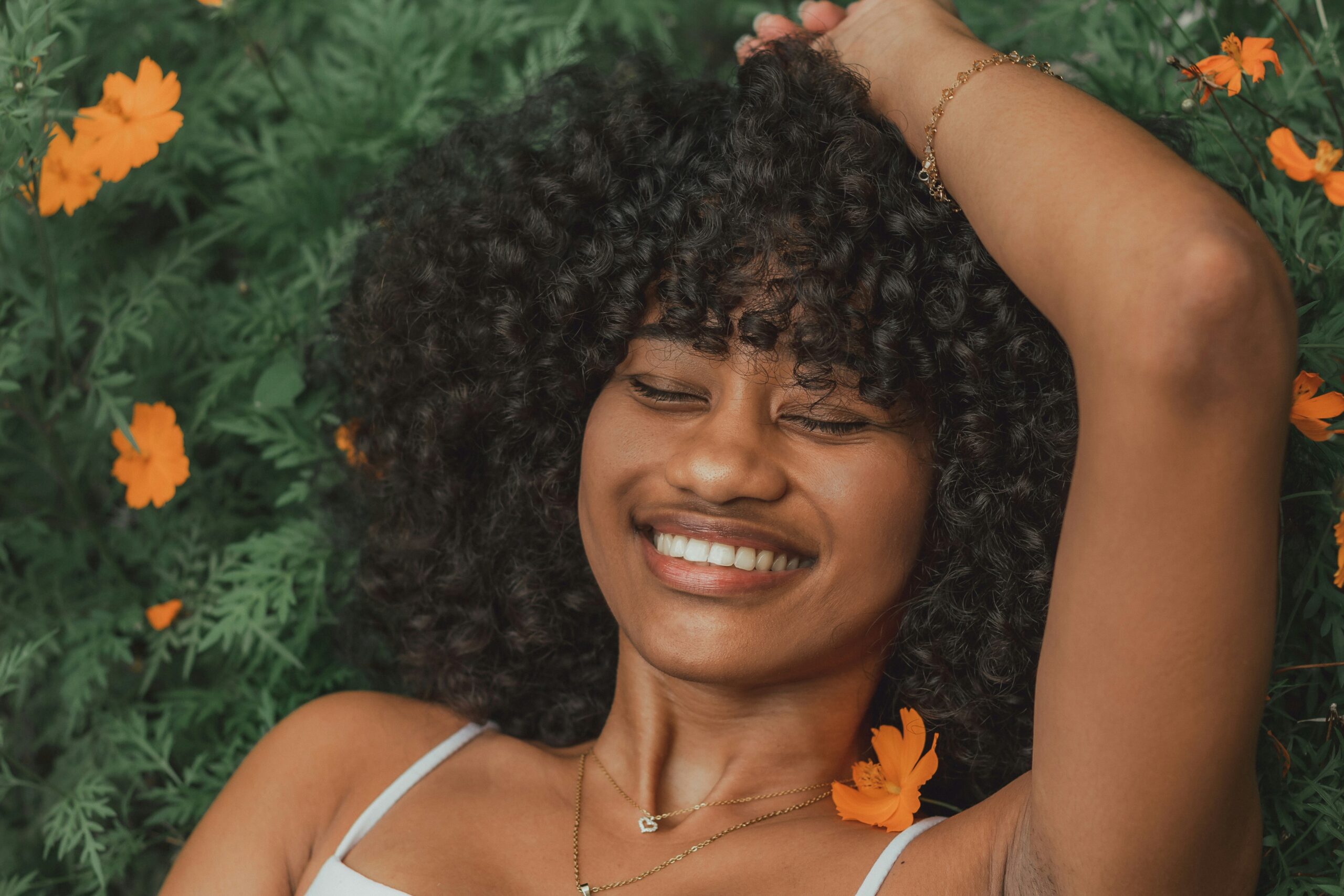 Woman laying in a field of orange flowers, smiling, eyes closed